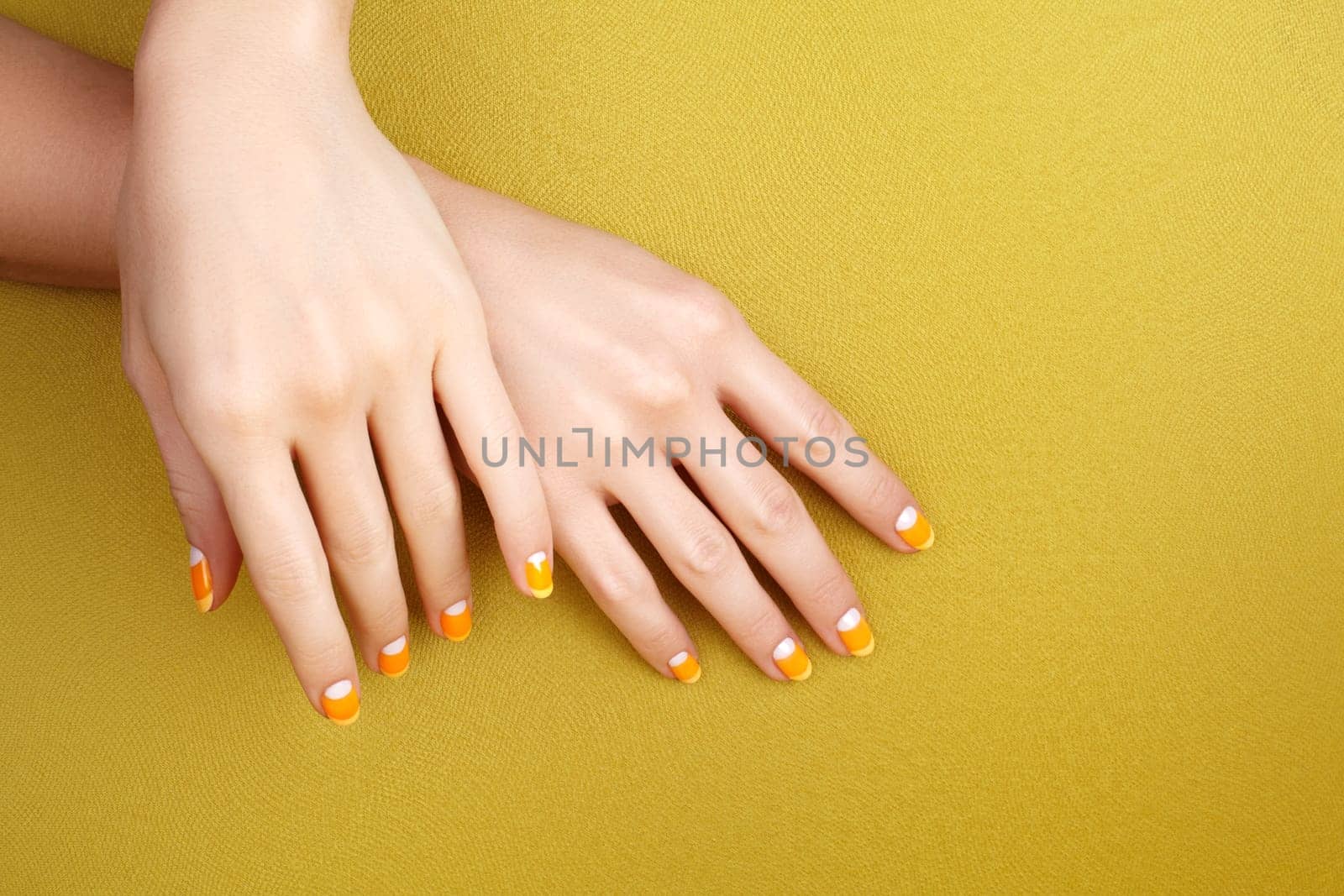 Beautiful Female Hands with bright Orange Manicure like Candy Corn on Yellow Background. Manicured Nails with Creative Gel Polish Design. Halloween Style