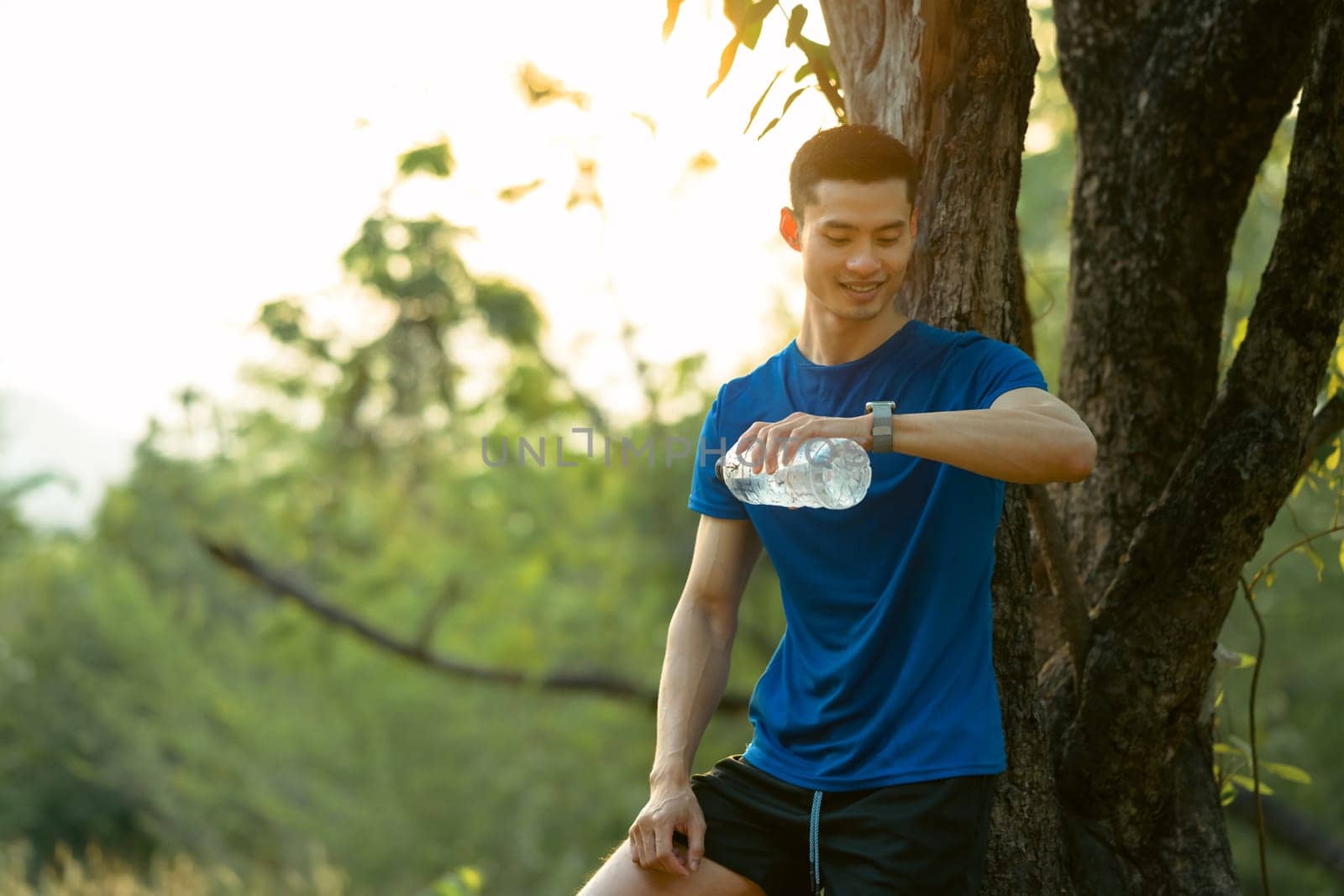 Portrait of male runner with bottle of water checking pulse on smartwatch after workout session at sunny morning.