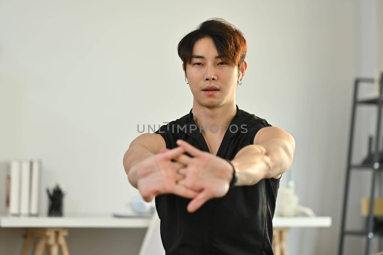 Shot of male athlete in fitness clothes doing stretching exercise, preparing for morning workout at home by prathanchorruangsak