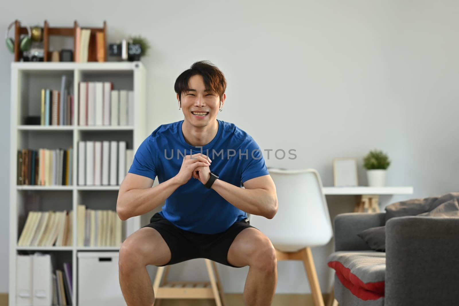 Sporty male in sportswear working out in the morning at home, doing squats exercise.Healthy lifestyle concept.