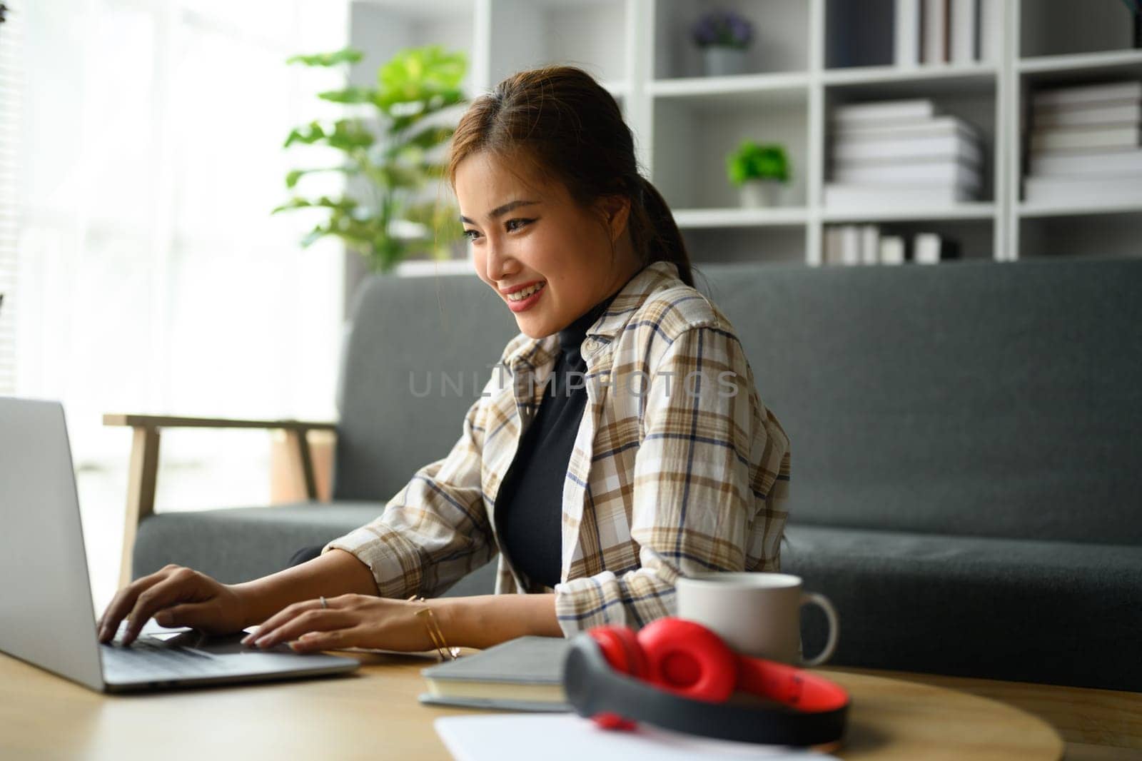 Charming millennial woman communicating in social media, checking email on laptop computer at home by prathanchorruangsak