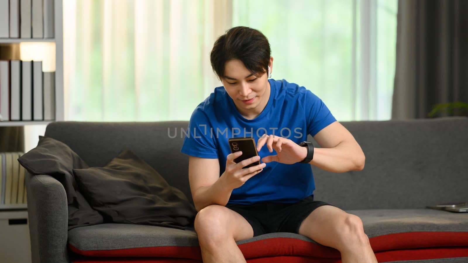 Casual millennial asian man using smartphone communication in social media while sitting on couch at home.
