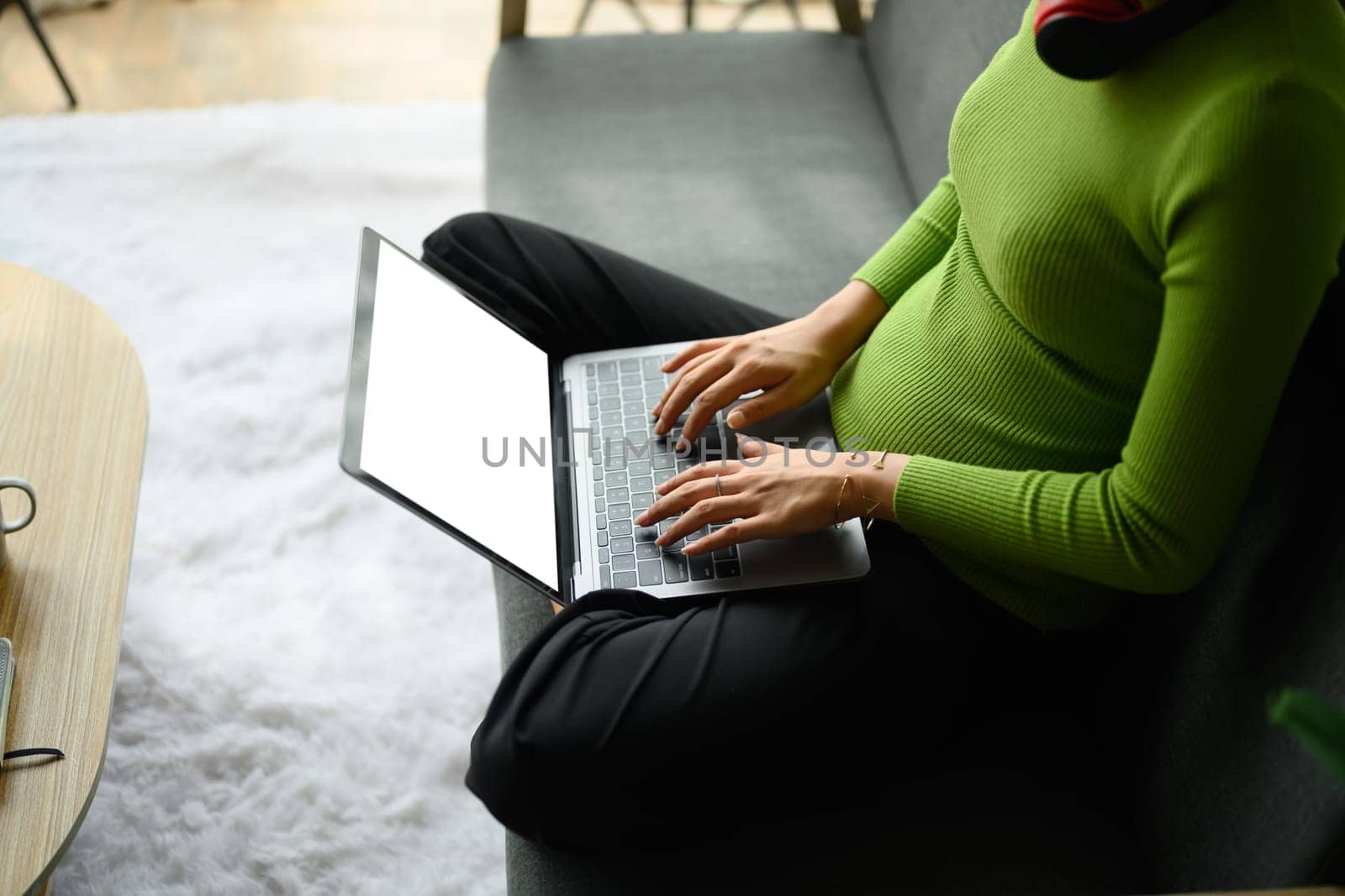 Cropped image of young woman dressed in green sweater sitting on couch and using laptop. Technology and communicating by prathanchorruangsak