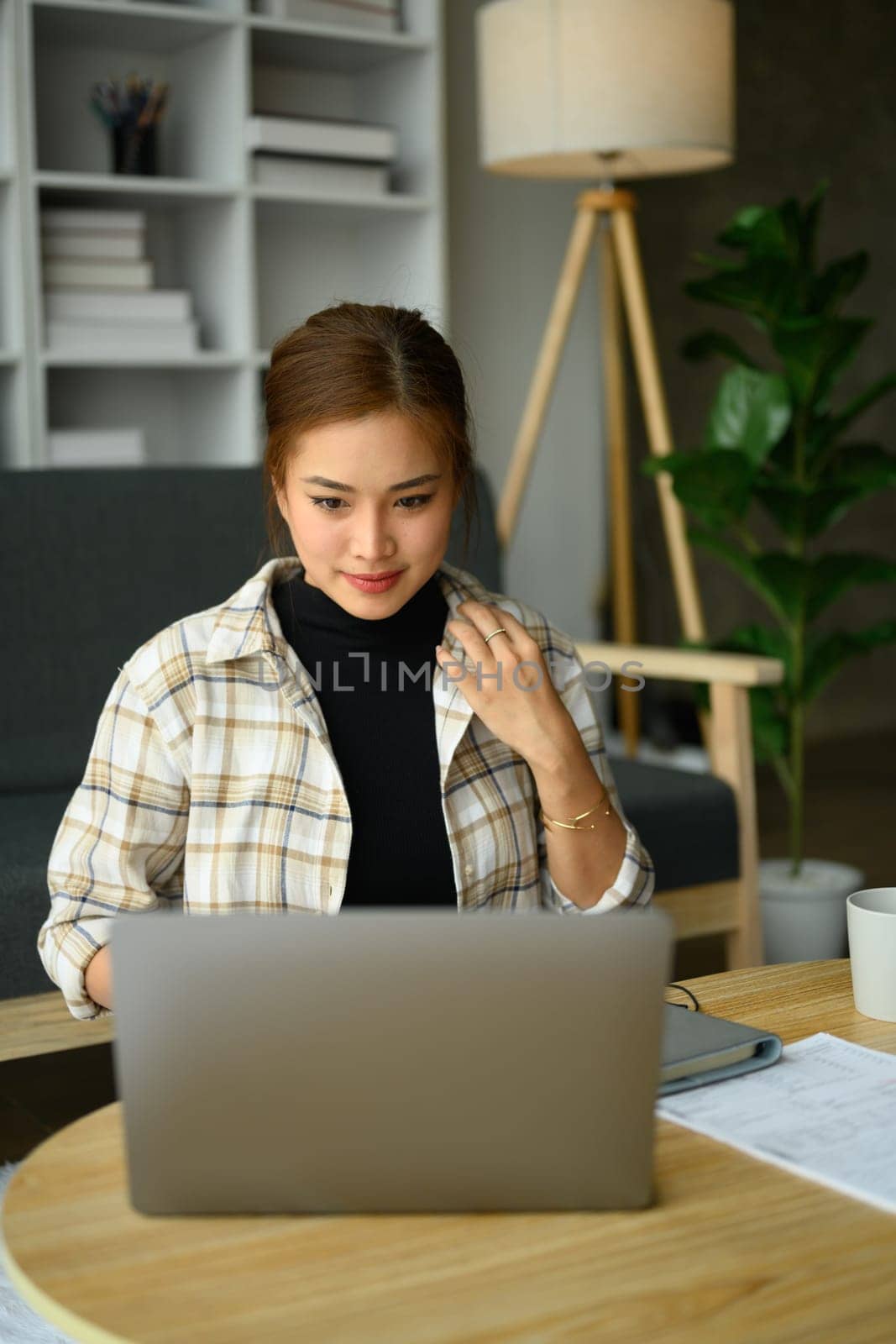 Image of beautiful young woman sitting in cozy living room, checking email or working online on laptop computer by prathanchorruangsak