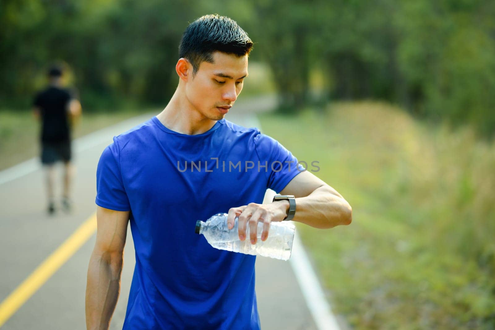 Athletic man monitoring fitness training on smartwatch during morning workout. Fitness, sport and healthy lifestyle concept by prathanchorruangsak