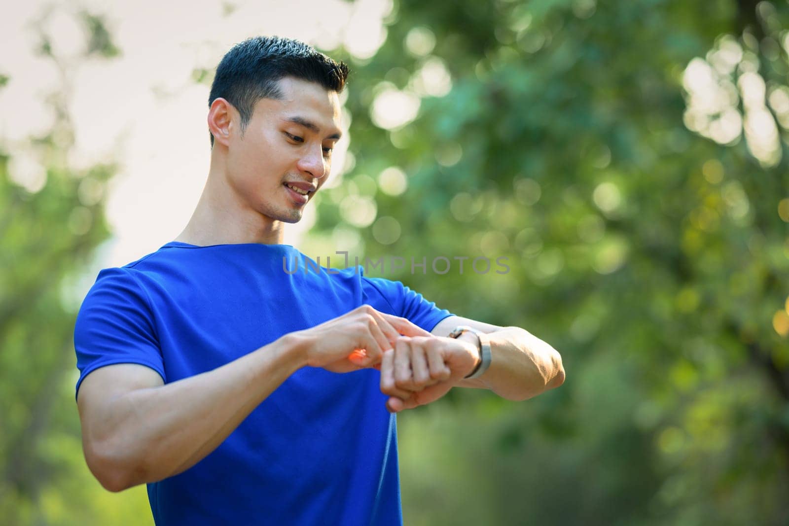 Handsome male runner checking smartwatch to monitor training results. Technology health, wellness concept by prathanchorruangsak