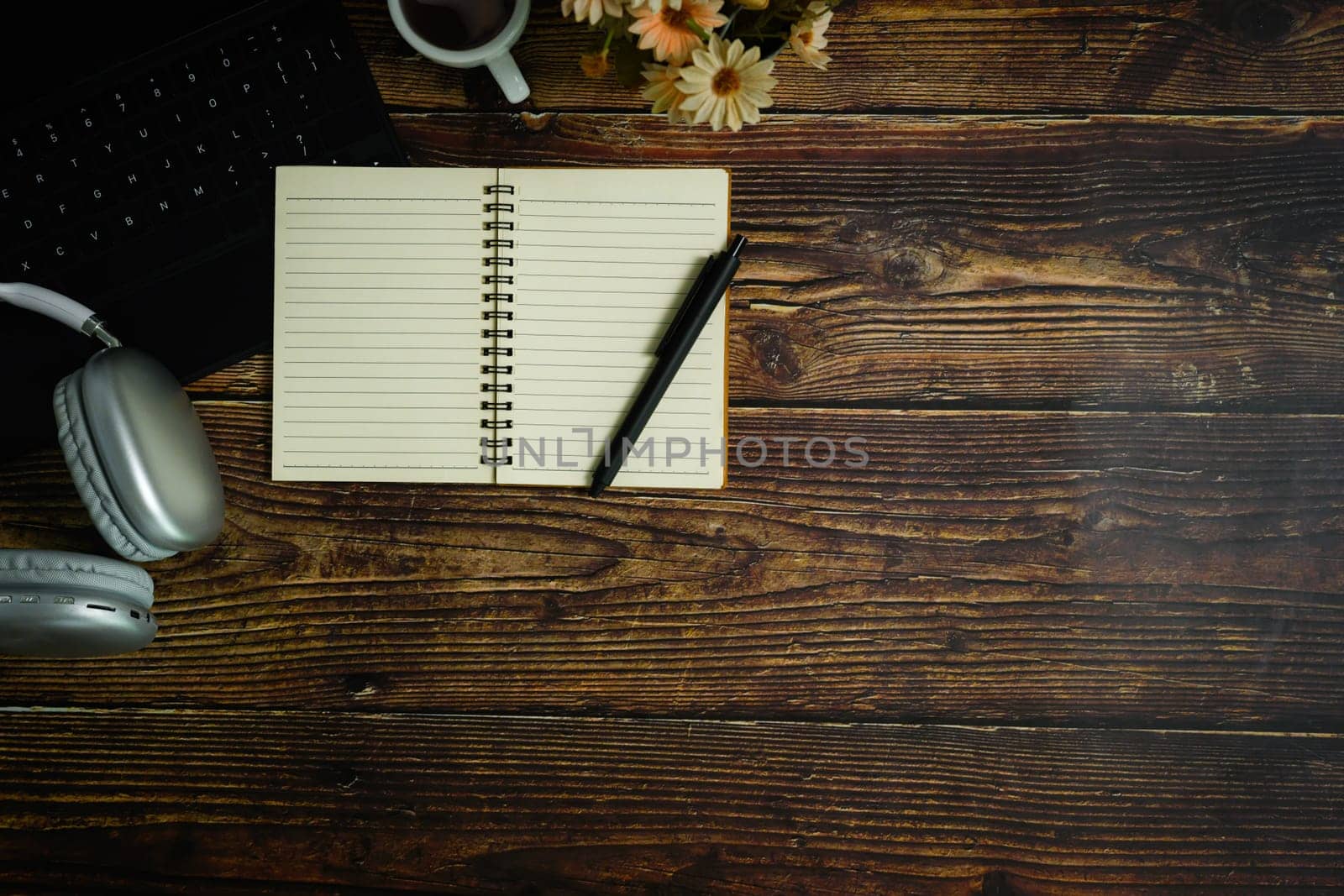 Top view of blank spiral notepad, pen, headphone and coffee cup on wooden table.