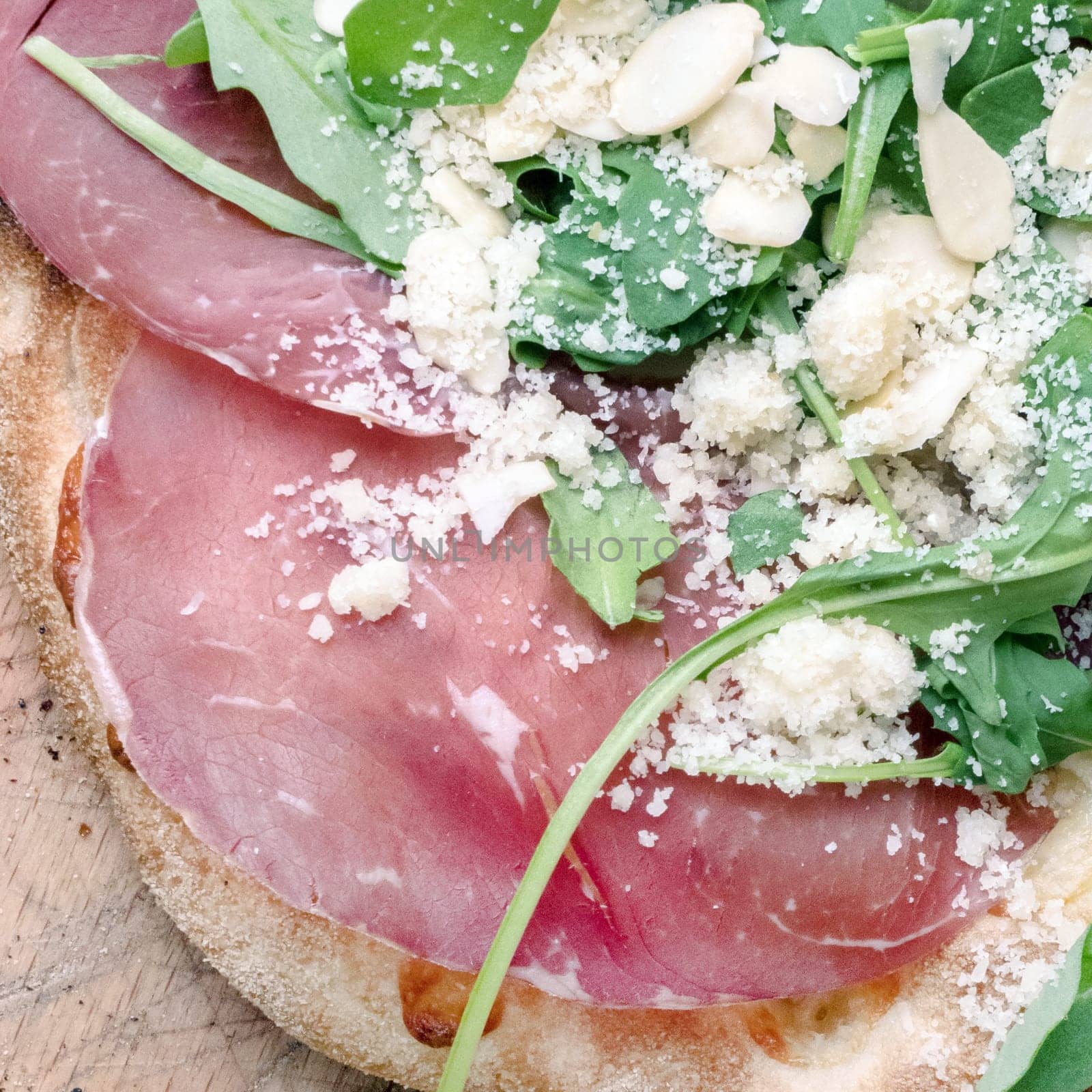 Pizza topping ideas. Gourmet pizza with mozzarella, rocket, bresaola, parmesan and almonds. Top view.