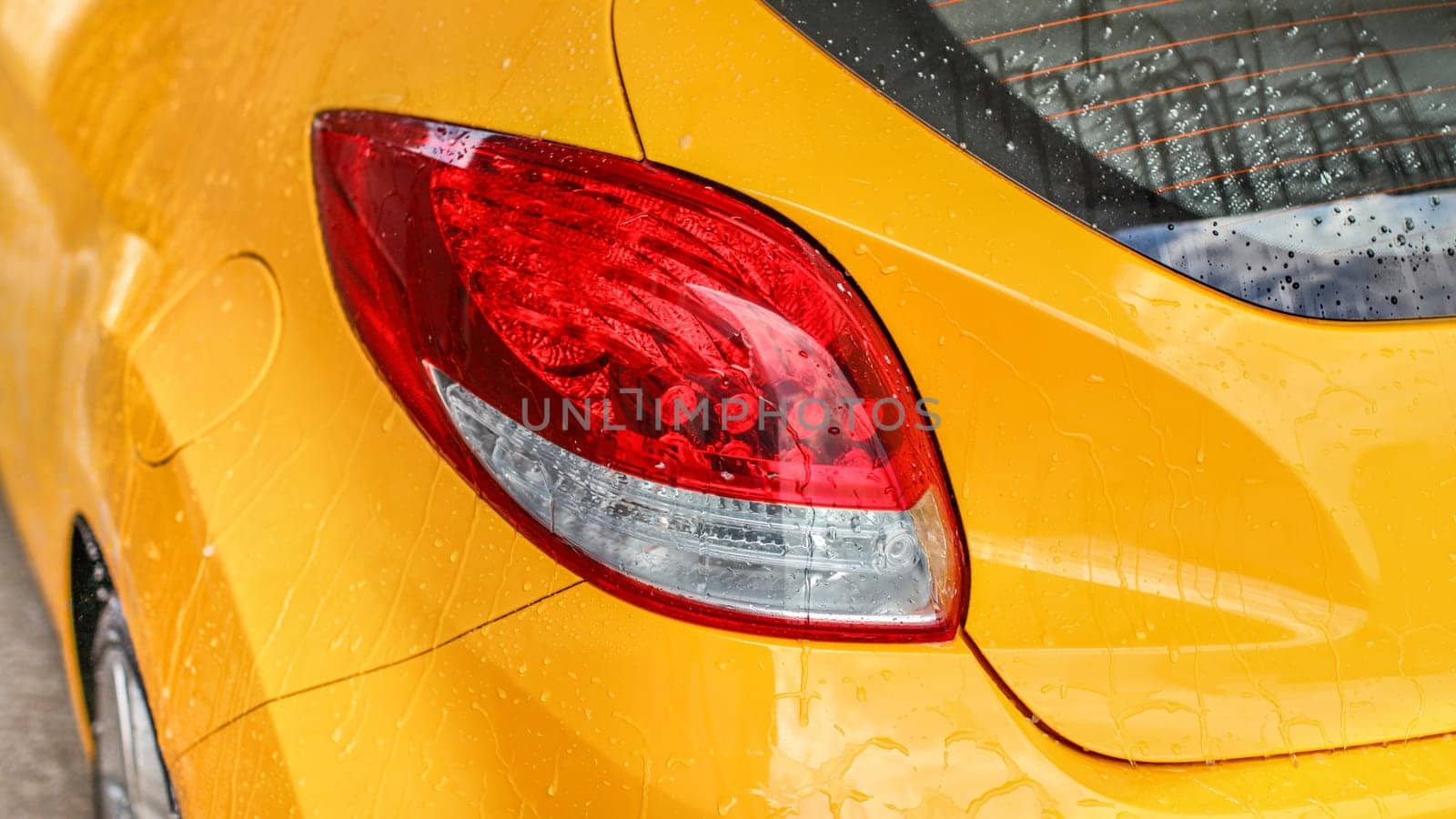 Rear light of yellow car covered with water when washed in carwash.