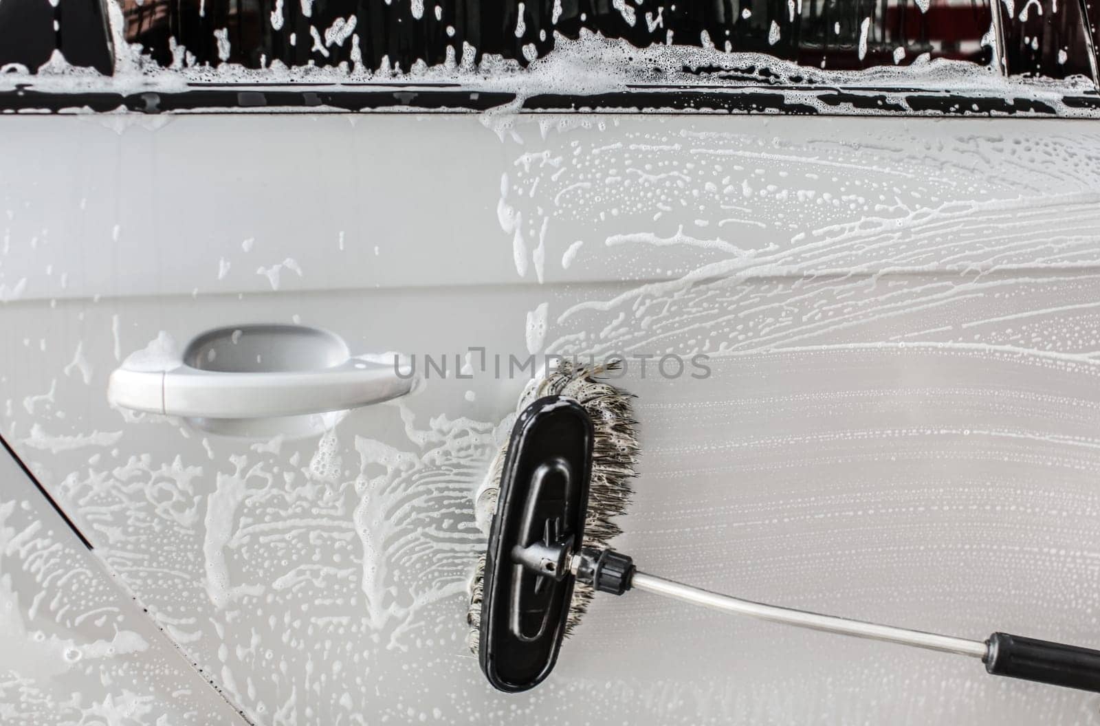 Side of silver car washed in self service carwash, brush cleaning shampoo foam.