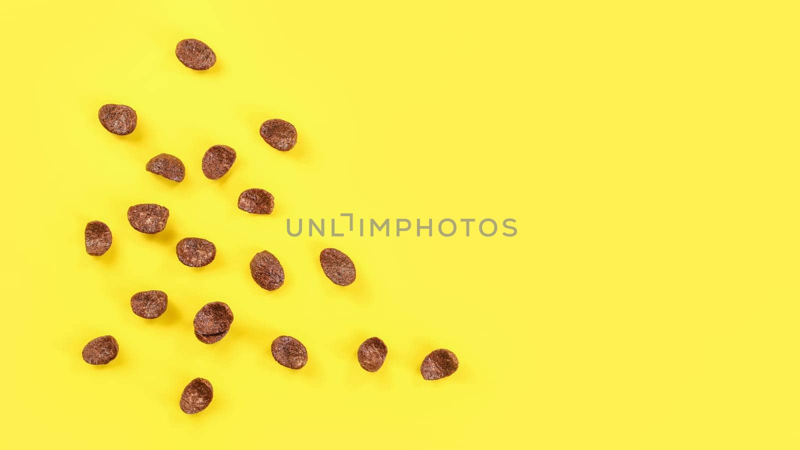 Tabletop view chocolate corn flakes scattered on yellow board, space for text on right side.