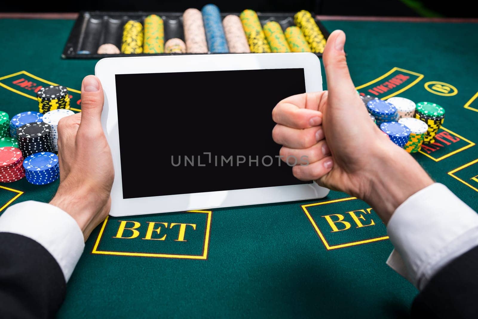 casino, online gambling, technology and people concept - close up of poker player with playing cards, tablet and chips at green casino table. first-person view.