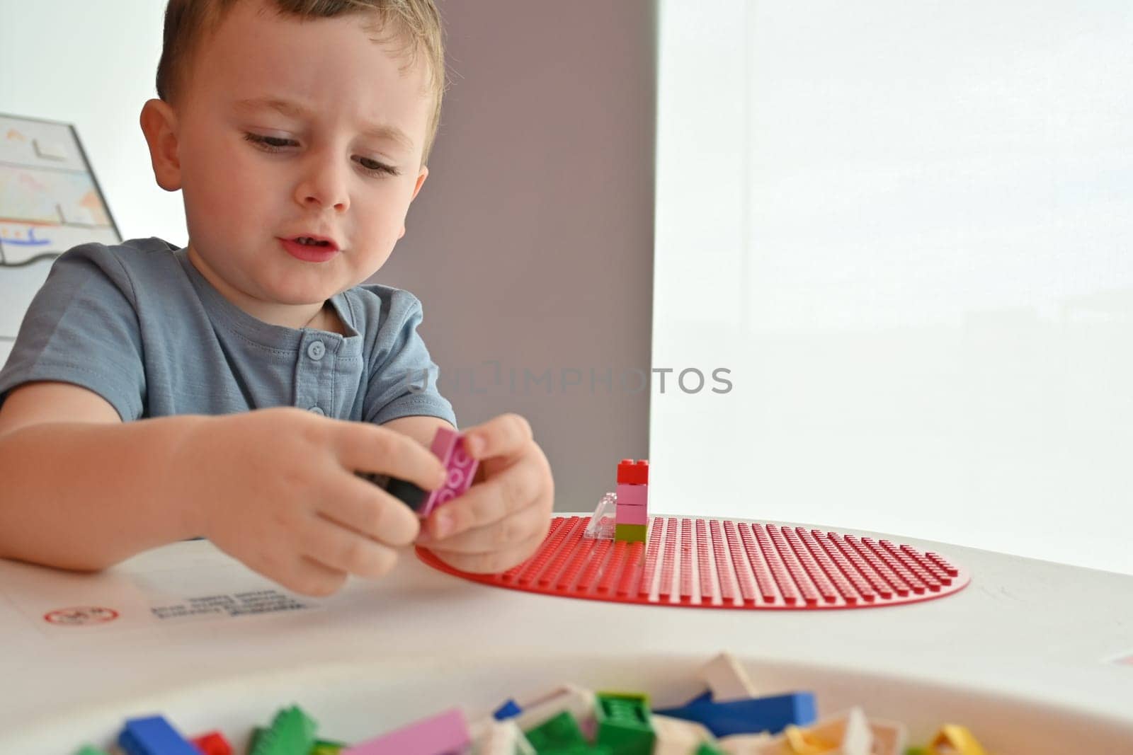 Little child playing with lots of colorful plastic toys indoor, building different cars and objects.