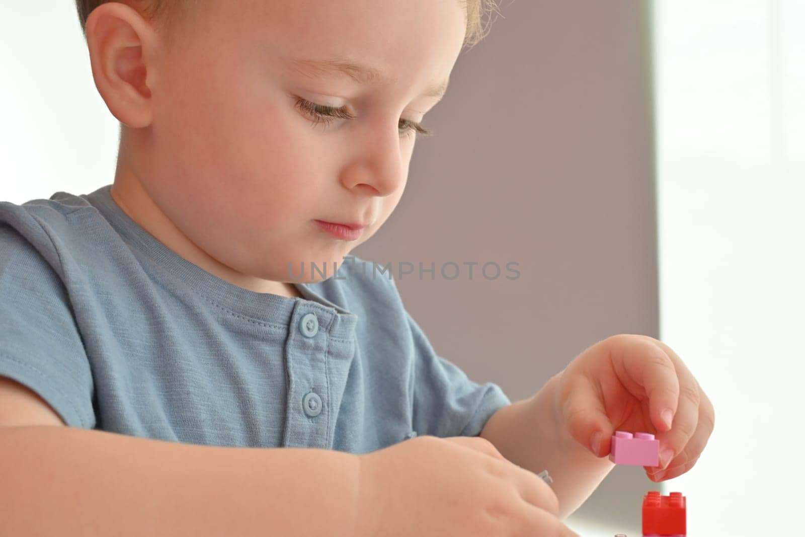 Little child playing with lots of colorful plastic toys indoor, building different cars and objects.