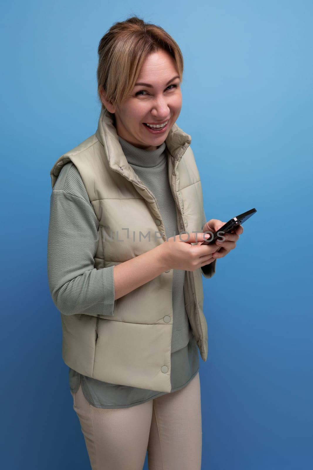 sociable blond 30 year old woman in casual clothes communicates using an online connection on a smartphone.