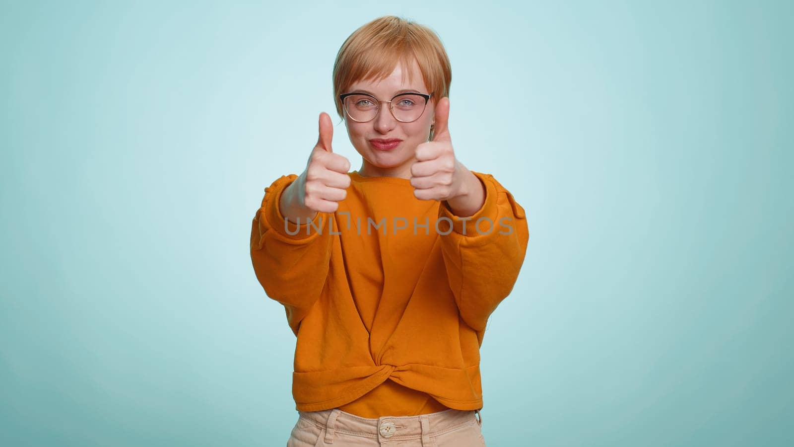 Like. Young woman raises thumbs up agrees with something or gives positive reply recommends advertisement likes good idea. Pretty short haired blonde girl isolated alone on blue studio background