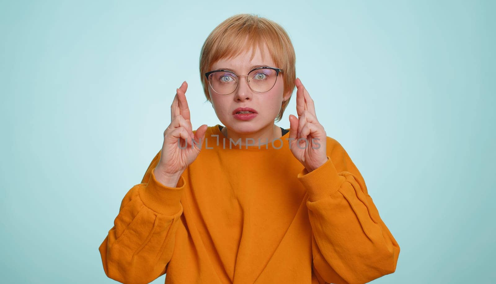 Excited shocked woman crossed fingers looking at camera asking for good luck news, wishing good exam results, dreaming about win victory in lottery jackpot. Girl isolated on yellow studio background