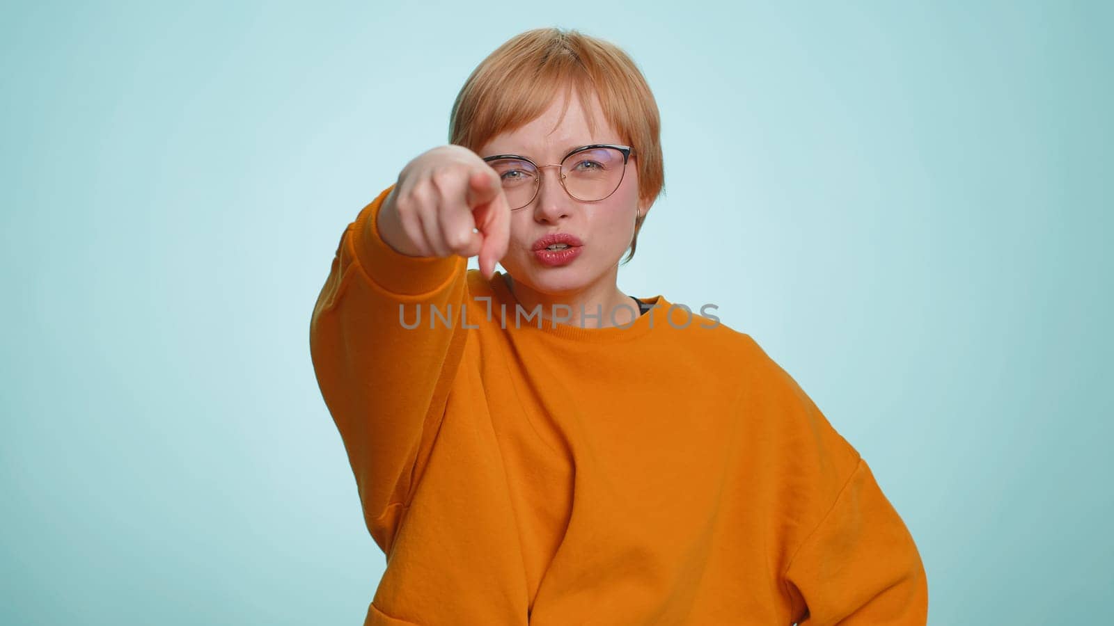 Hey you. Young woman smiling excitedly and pointing to camera, choosing lucky happy winner, indicating to awesome you. Pretty short haired blonde girl isolated alone on blue studio wall background