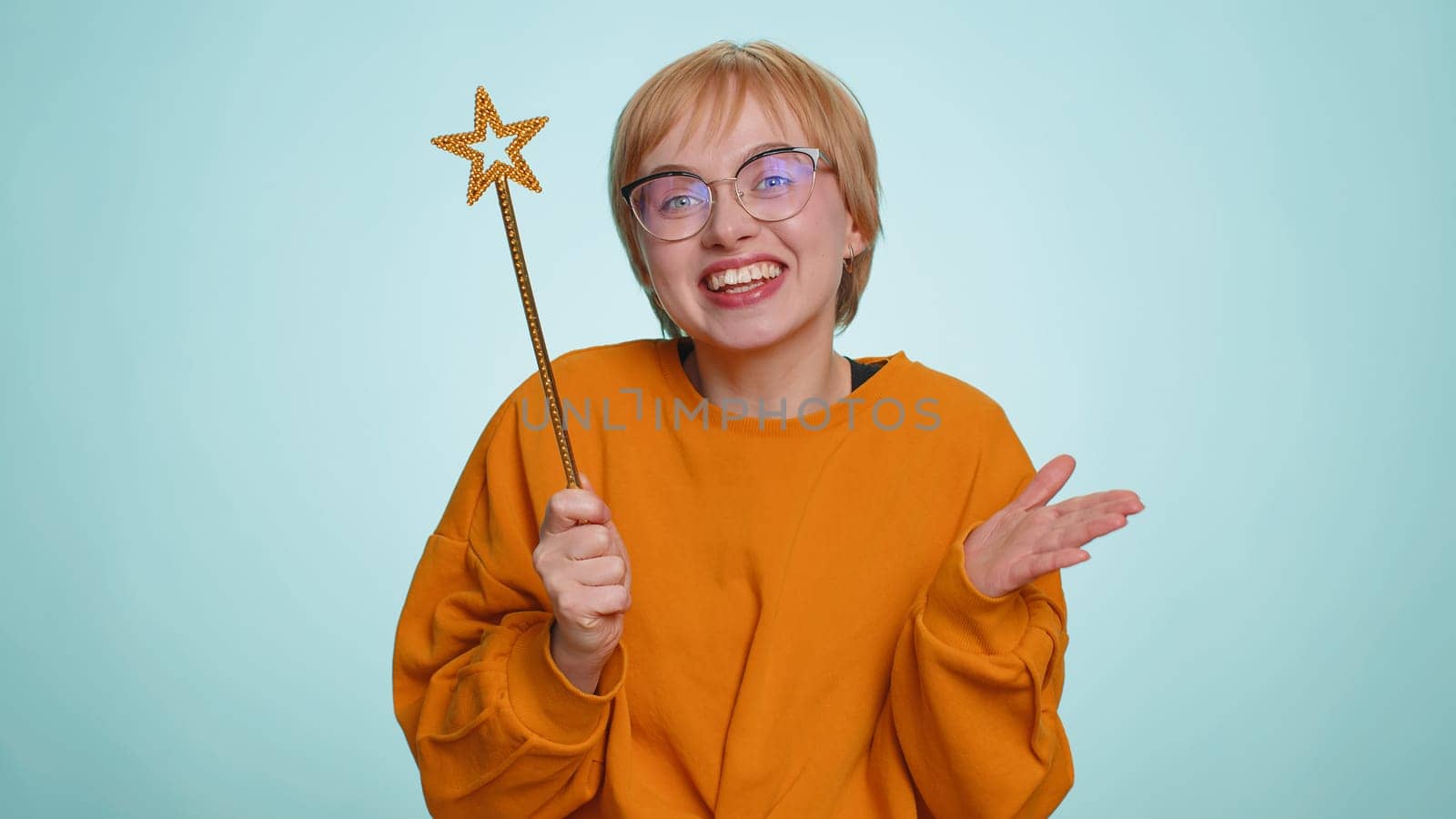Magician witch young woman gesturing with magic wand fairy stick, making wish come true, casting magician spell, advertising holidays sale discount. Pretty girl isolated on blue studio background