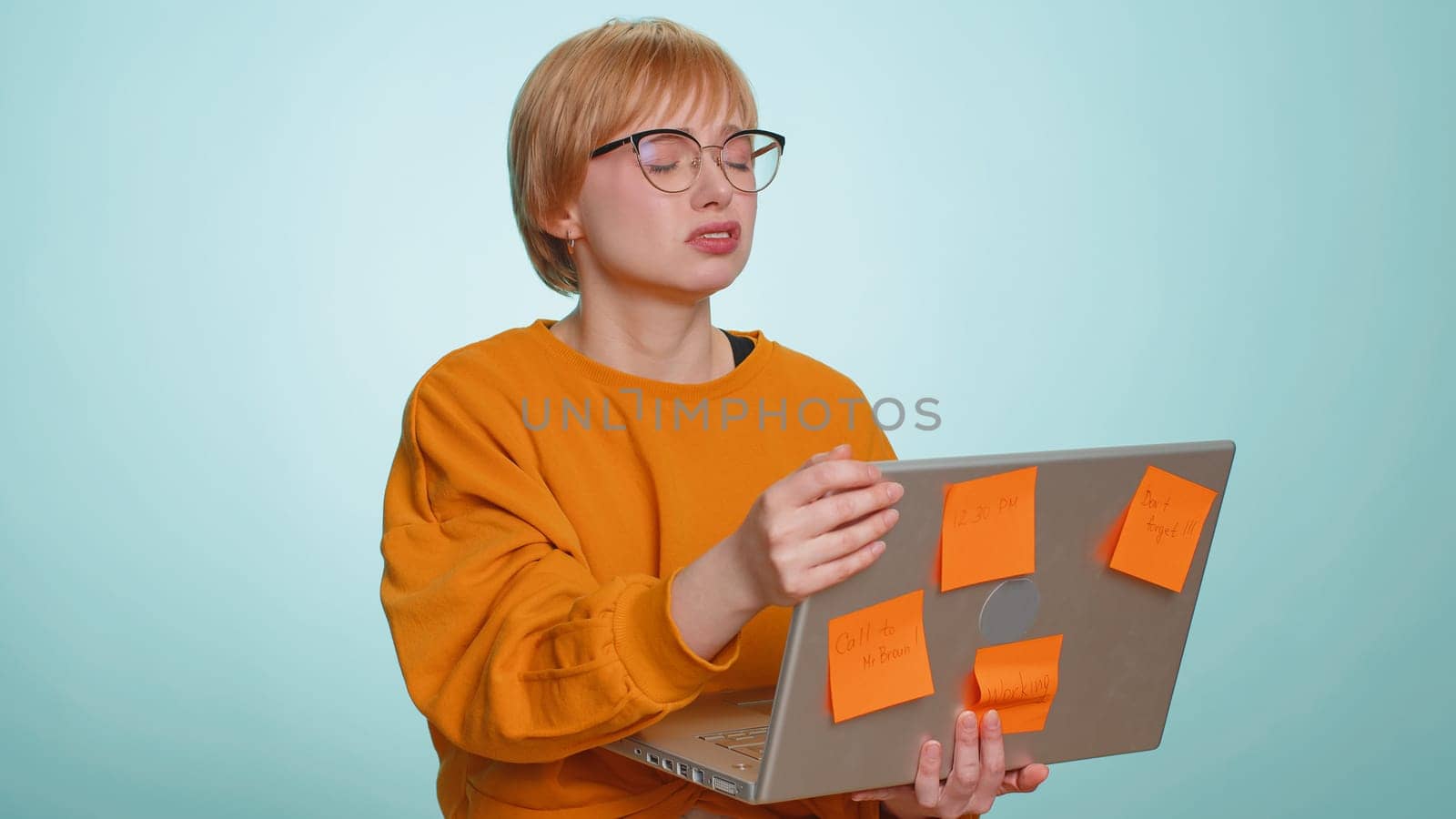 Exhausted freelancer woman in glasses with pasted sticker notes use laptop computer having concentration problem creative crisis. Nervous girl confused by big routine work loading on blue background