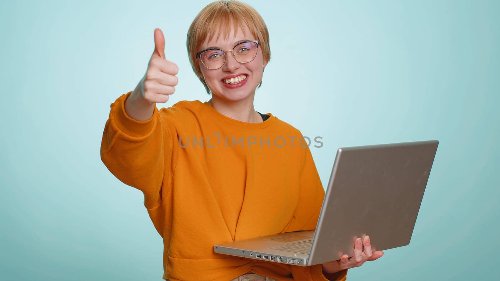 Excited happy young woman typing on laptop computer, working on project, enjoying results, winning lottery, celebrating success online shopping, win. Blonde girl isolated on blue studio background