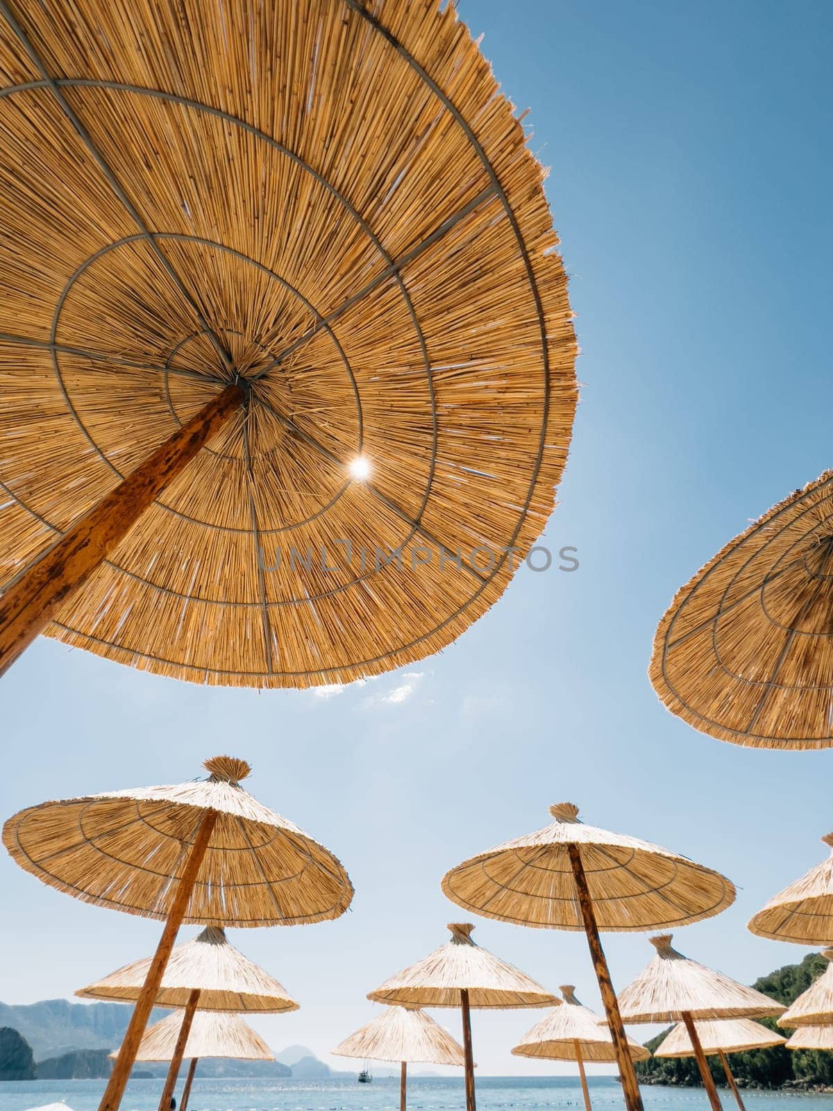 Straw sun umbrellas on the beach by the sea against the blue sky. High quality photo