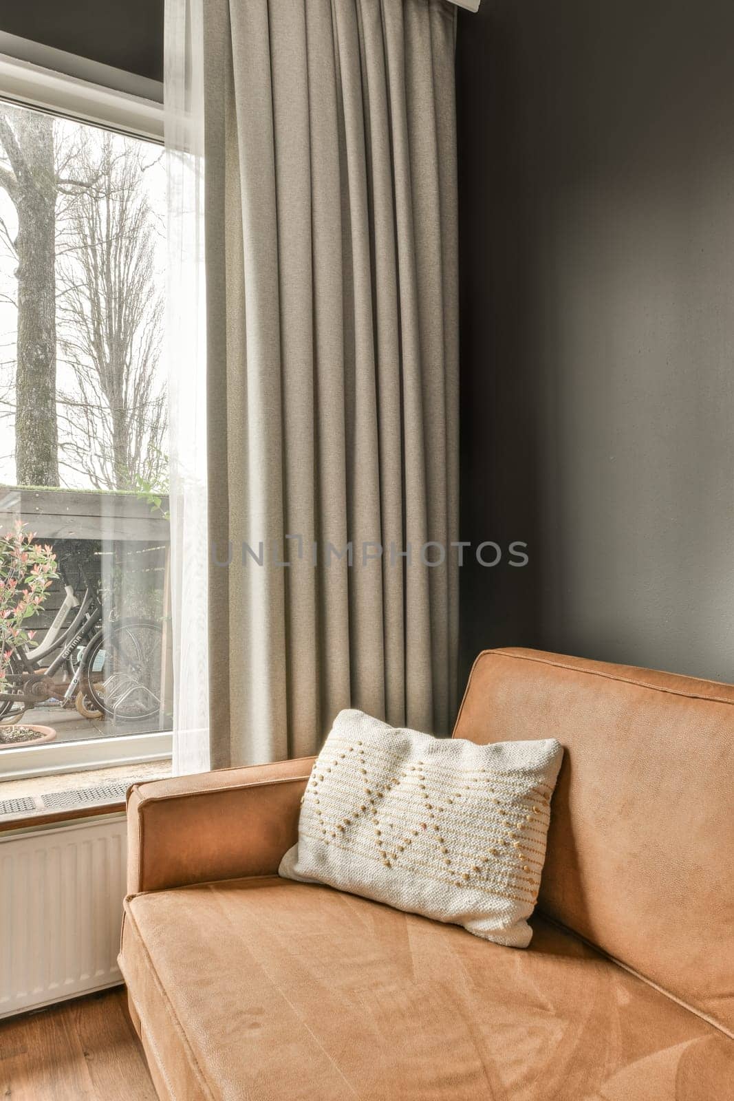 a couch in front of a window with curtains on the windowsilling it is brown and has a white throw pillow
