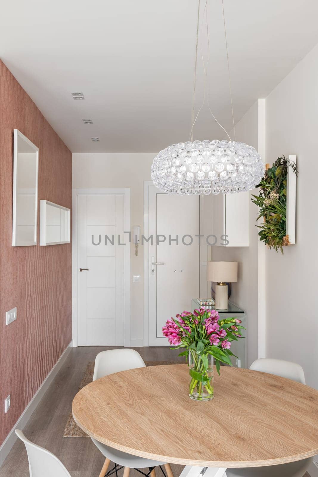 Small studio living room with a comfortable space zoning, table with flowers and a crystal chandelier on the background of the front door and stylish decor accessories. Cozy small apartment concept.