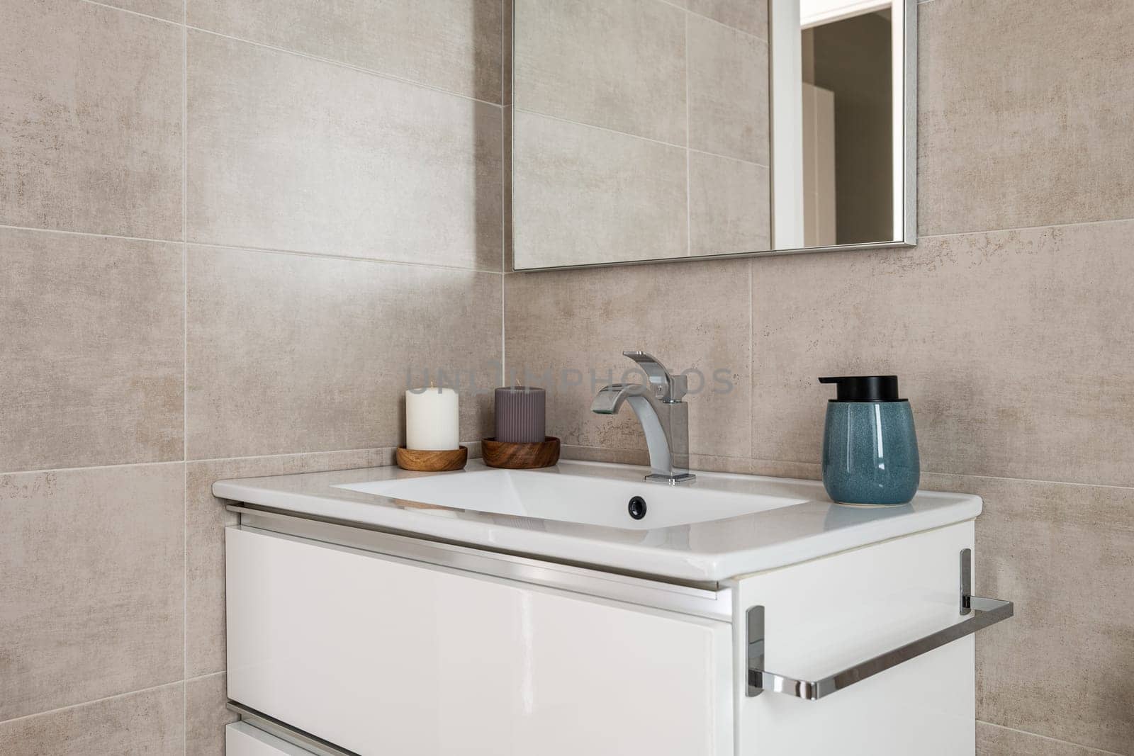 Comfortable bathroom with sink and mirror with beige tiles and natural lighting. The concept of a bathroom in hotel or apartment after a purchase with a mortgage.