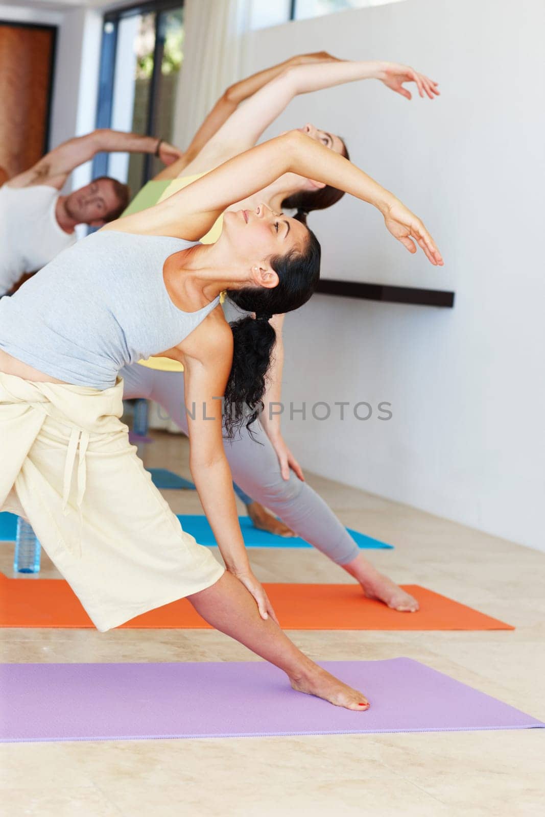 Stretching their way to health. a diverse group of yoga students stretching sideways during a yoga lesson. by YuriArcurs