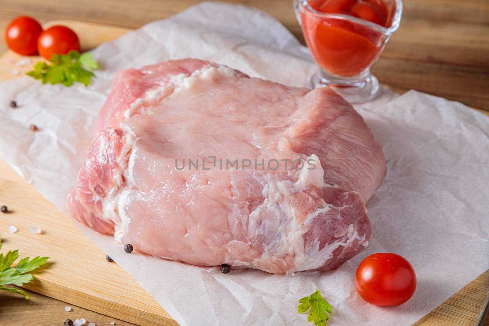 A piece of raw pork meat on a cutting board. Tomatoes, ketchup