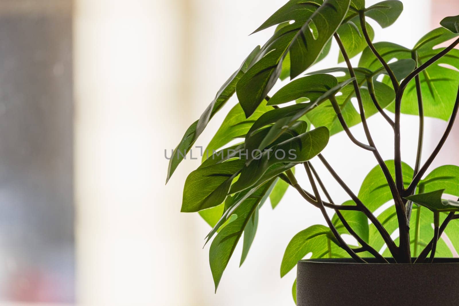 Green artificial flower with a lot of plastic leaves in gray concrete flower pot