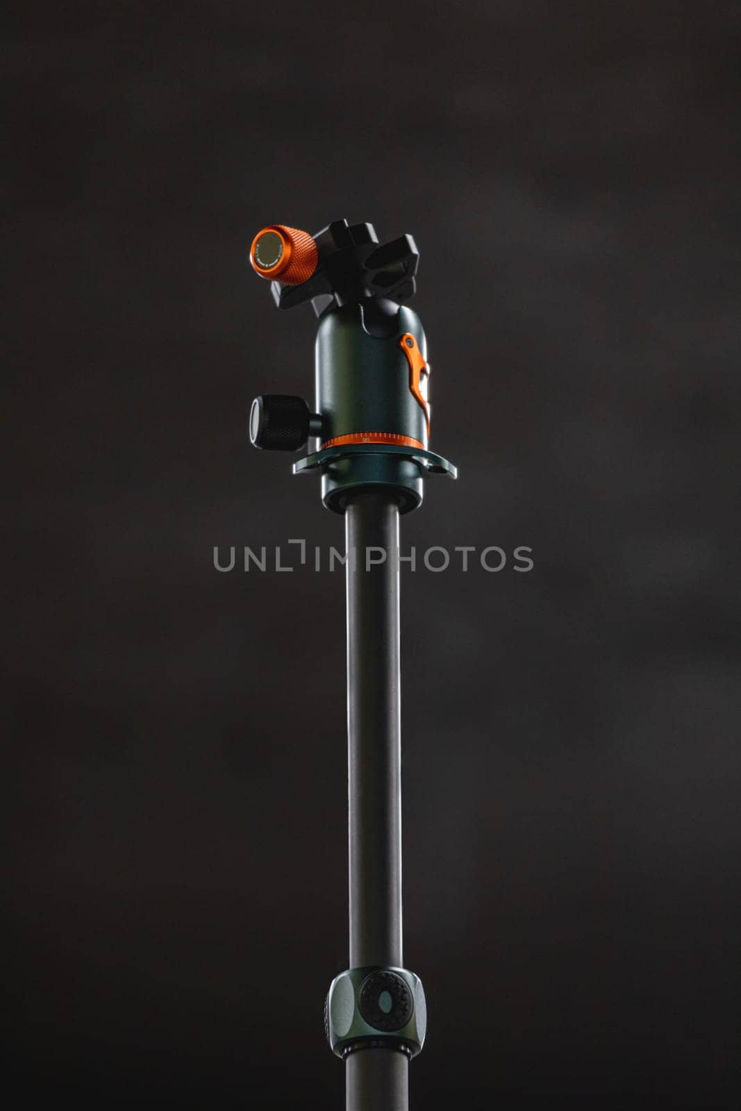 Gray central column of photo tripod with green and orange ballhead on top