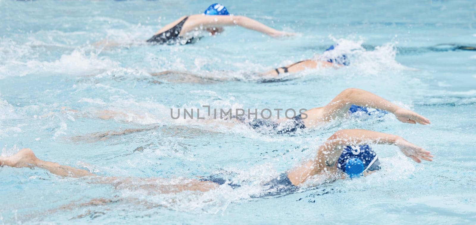 Swimming, water and race with a sports woman group in a pool for fitness, training or competition. Workout, exercise and swimmer with an athlete team racing for cardio or endurance during a swim by YuriArcurs