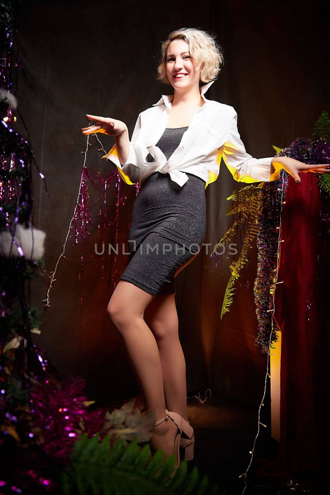 An elegant blonde girl in white blouse in a room decorated for Christmas or new year with a background, tinsel and light garlands