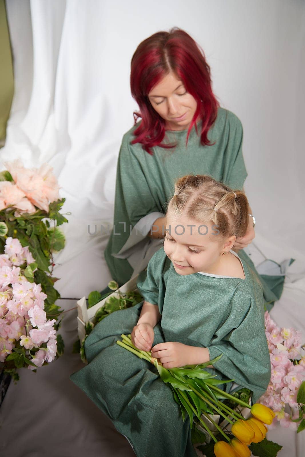 Amazing pretty mother and daughter having fun with flowers in 8 March or in Mother's day. Red haired mom and small little blonde girl having lovely free time on white background by keleny