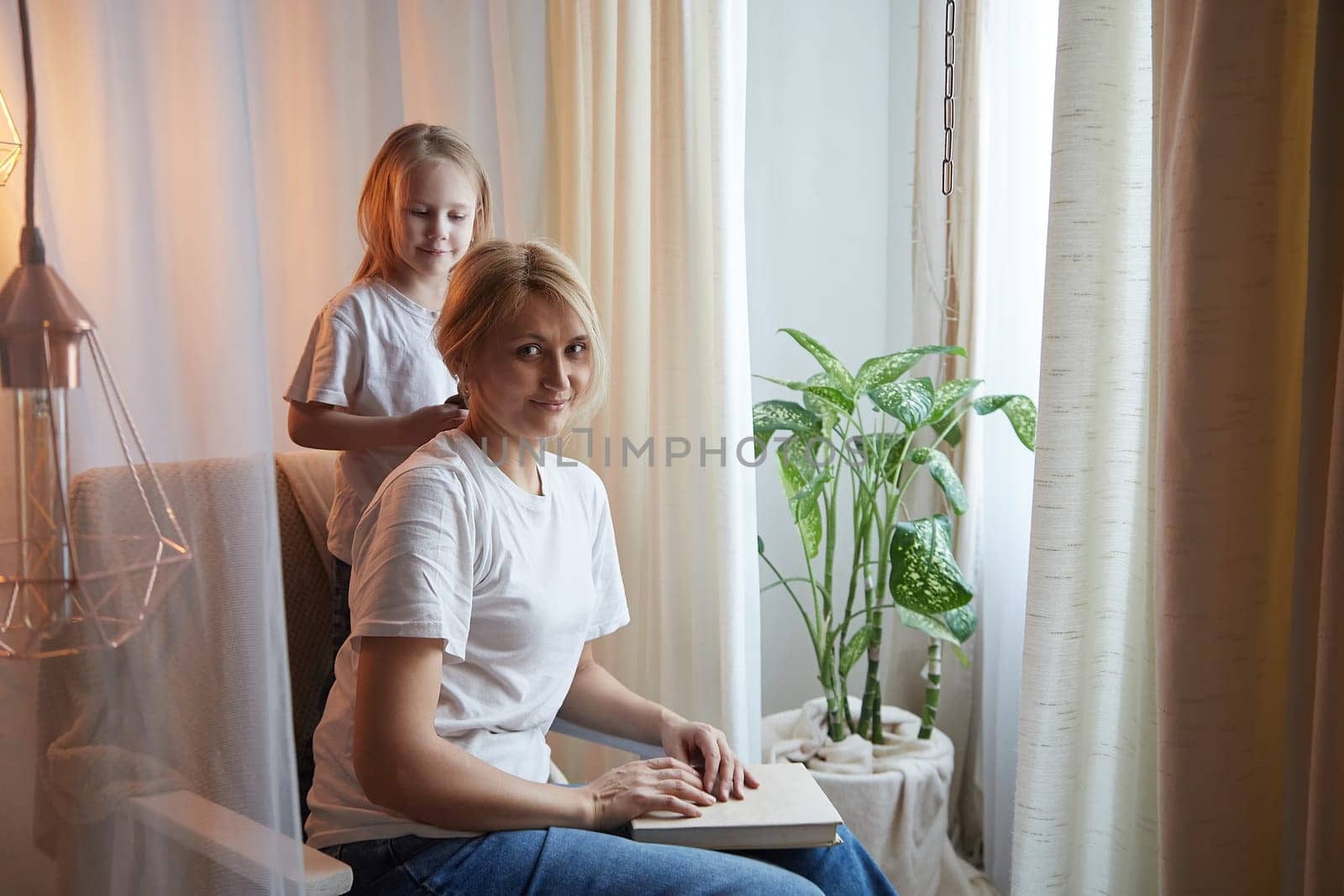 Happy loving family with mother and daughter in living room. Woman mom and small child girl playing and having convercation inside of the home by keleny