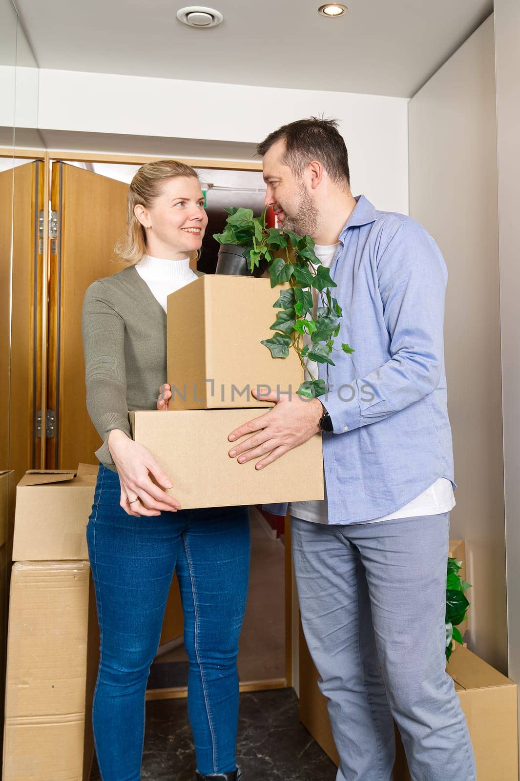 Happy couple moving in their new apartment carrying cardboard boxes. Young family moving in concept by PhotoTime