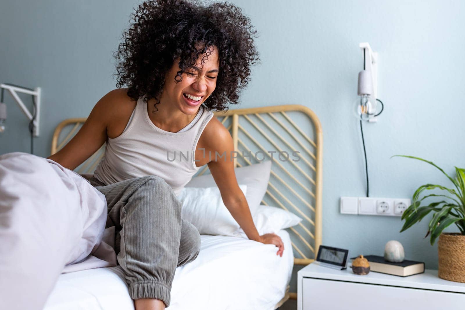 Happy young multiracial latina woman getting out of bed in the morning laughing. Happiness. by Hoverstock