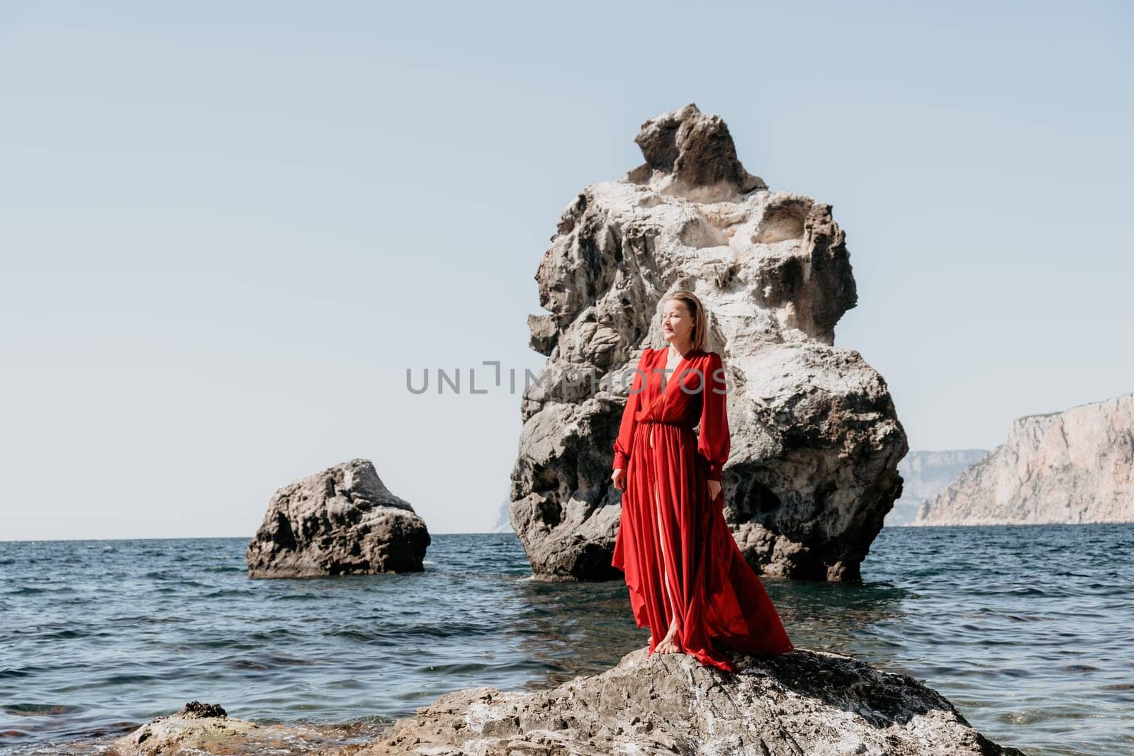 Woman travel sea. Young Happy woman in a long red dress posing on a beach near the sea on background of volcanic rocks, like in Iceland, sharing travel adventure journey