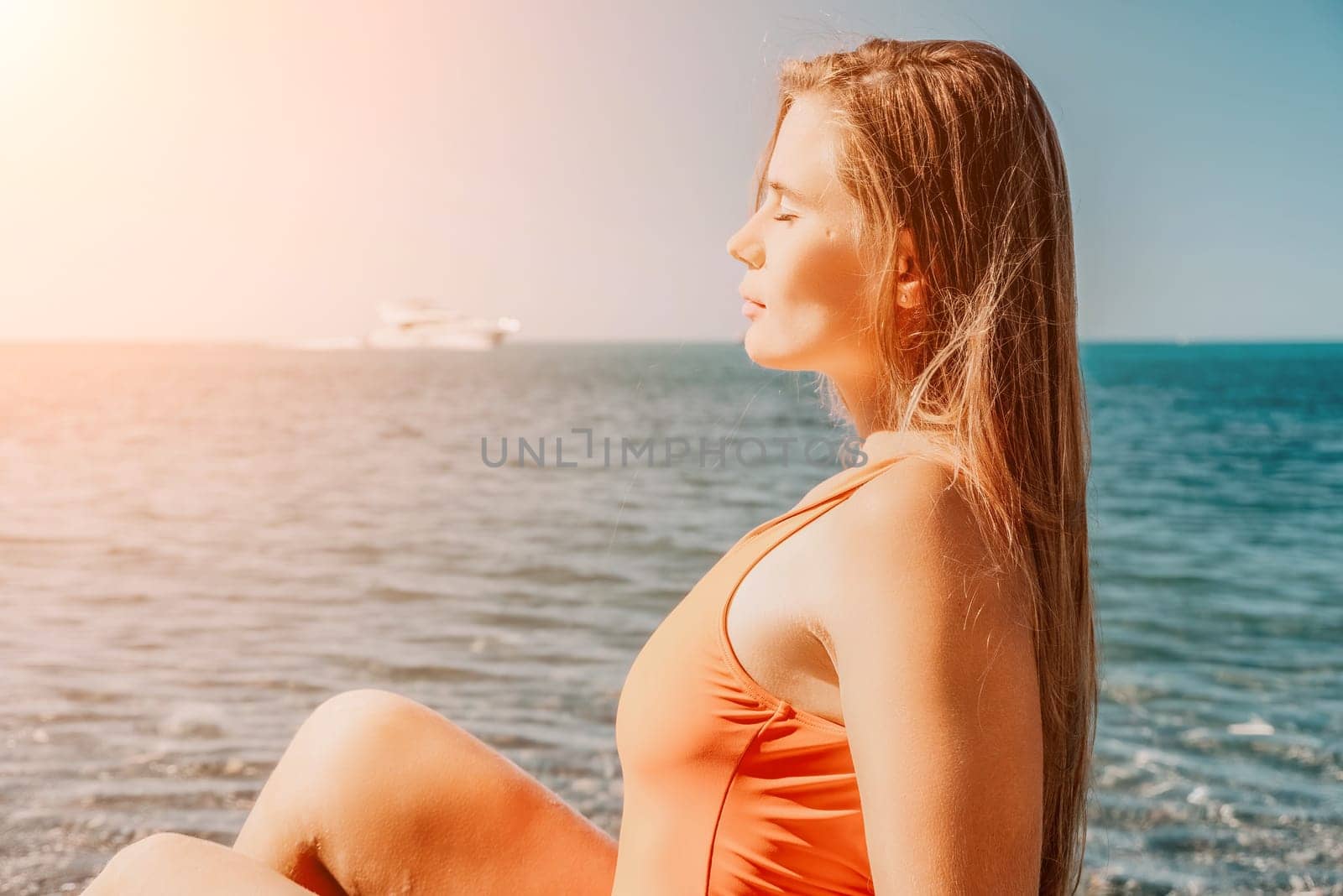 Young woman in red bikini on Beach. Girl lying on pebble beach and enjoying sun. Happy lady with long hair in bathing suit chilling and sunbathing by turquoise sea ocean on hot summer day. Close up by panophotograph