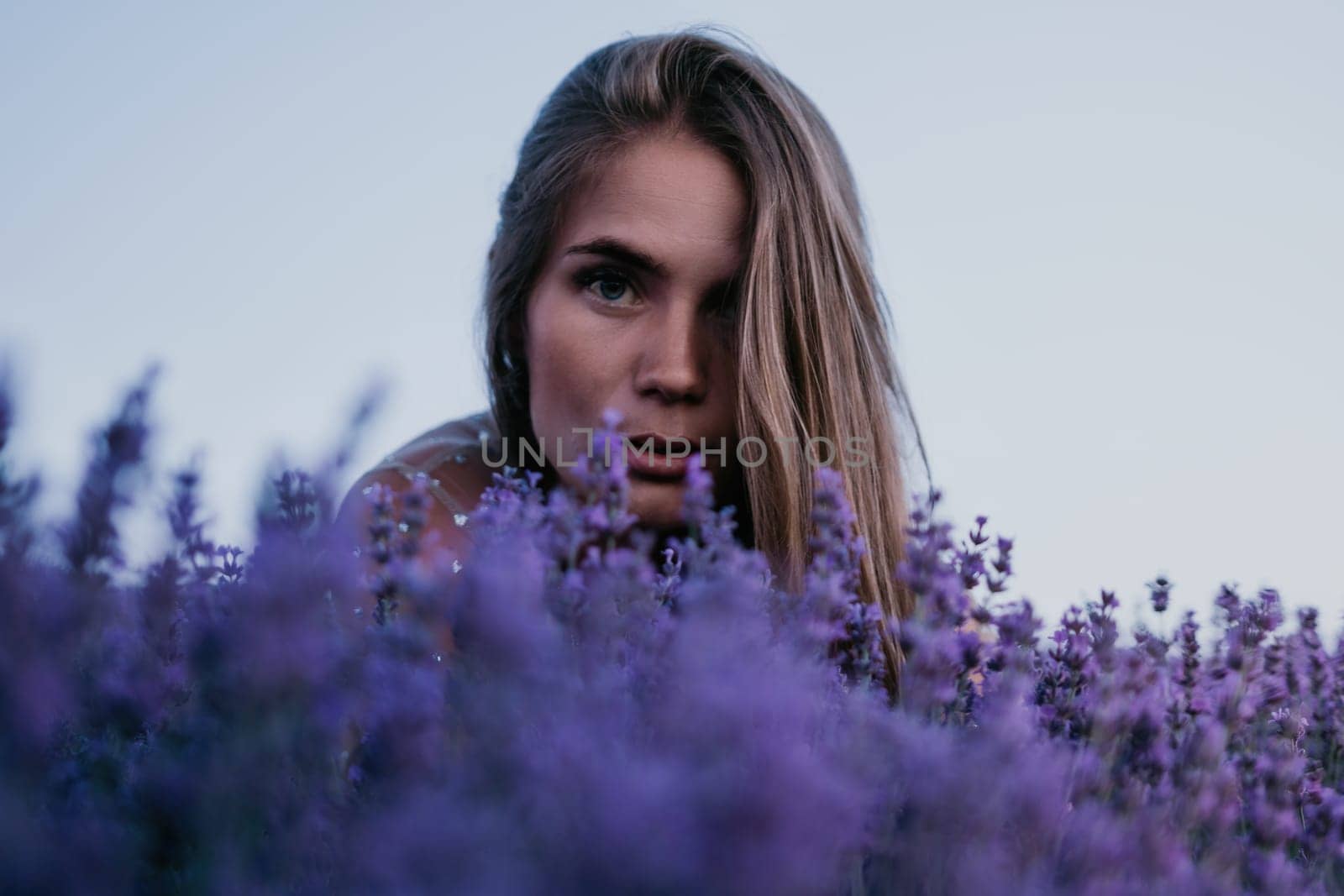 Close up portrait of young beautiful woman in a white dress and a hat is walking in the lavender field and smelling lavender bouquet.