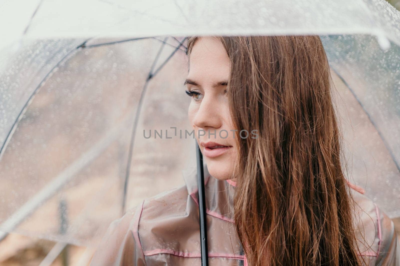 Woman rain umbrella. Happy woman portrait wearing a raincoat with transparent umbrella outdoors on rainy day in park near sea. Girl on the nature on rainy overcast day. by panophotograph