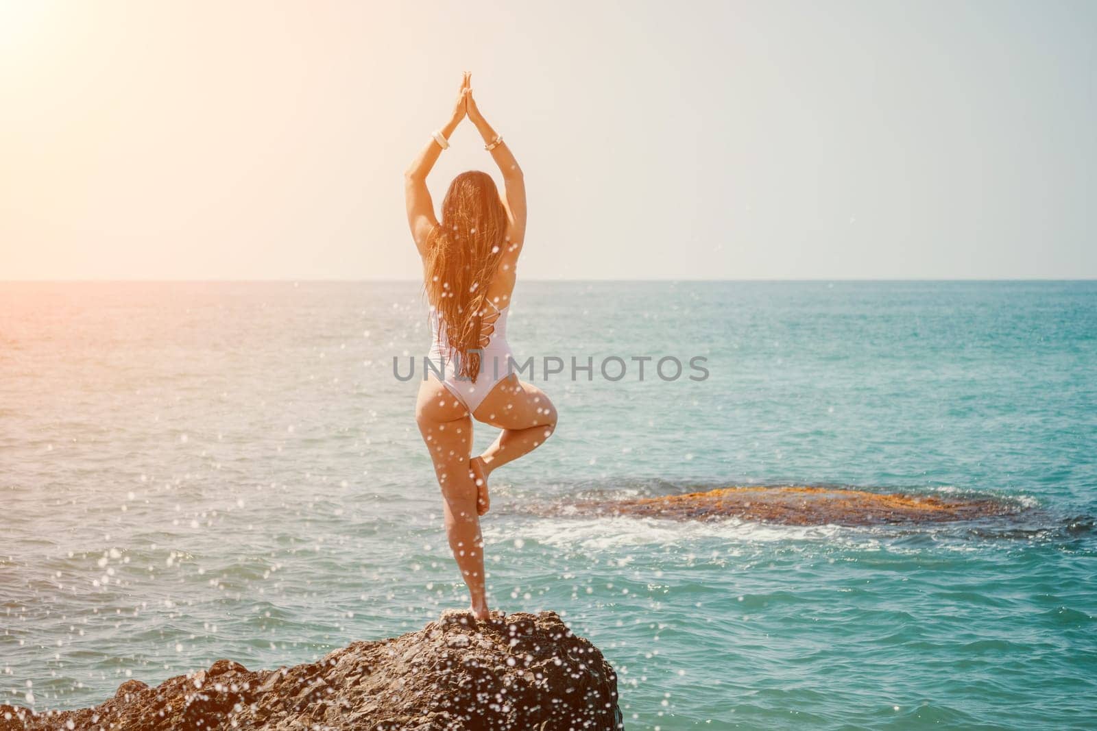 Woman sea yoga. Back view of free calm happy satisfied woman with long hair standing on top rock with yoga position against of sky by the sea. Healthy lifestyle outdoors in nature, fitness concept