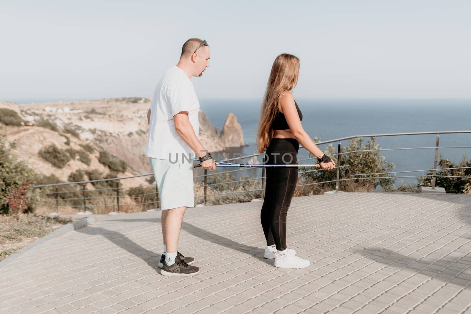 Happy Middle aged couple or friends practicing nordic walking in park near sea. Mature couple with trekking poles walking, practicing Nordic walking outdoors. Aging youthfully and sport concept.