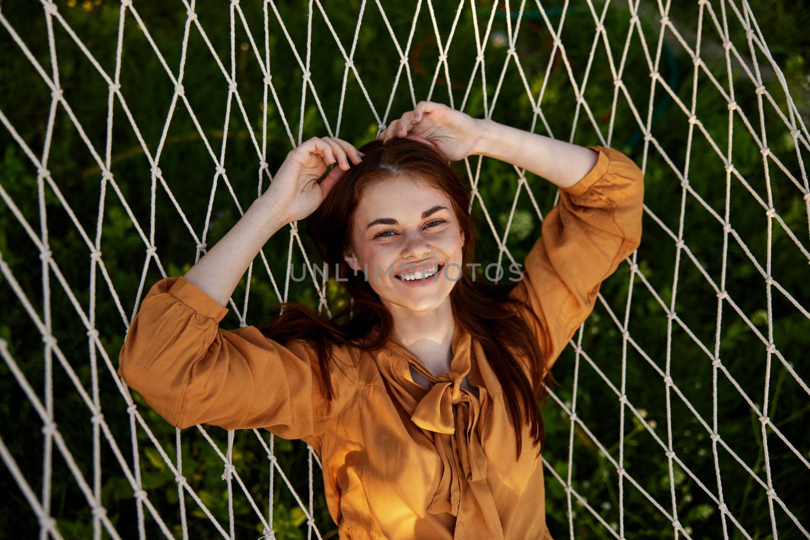a close horizontal photo from above of a happy, pleasantly smiling woman lying on a mesh hammock in nature on a sunny day. High quality photo
