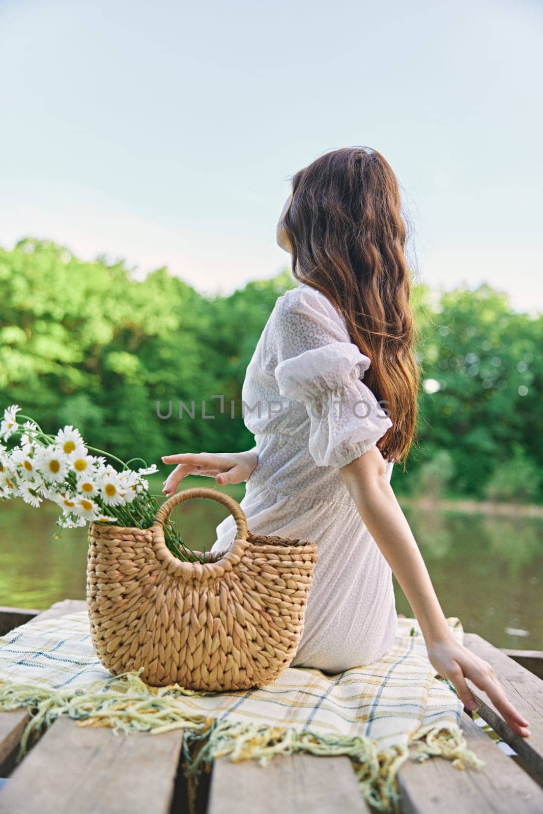 a woman with long well-groomed hair sits on the pier enjoying the view of the lake. High quality photo