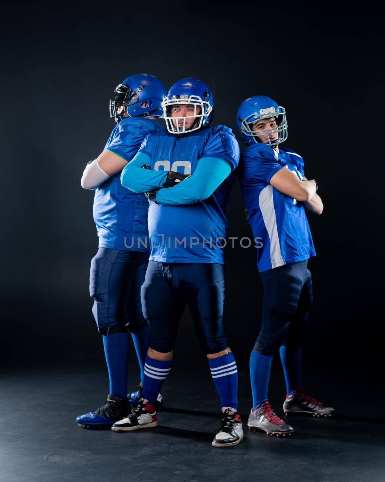 Portrait of three men in blue American football uniforms standing with their arms crossed over their chests on a black background