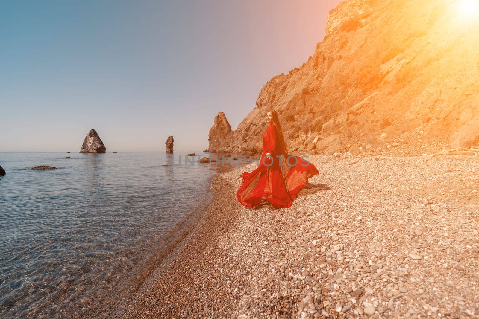 woman sea red dress Happy woman in a flying red dress and with long hair, stands on the seashore.