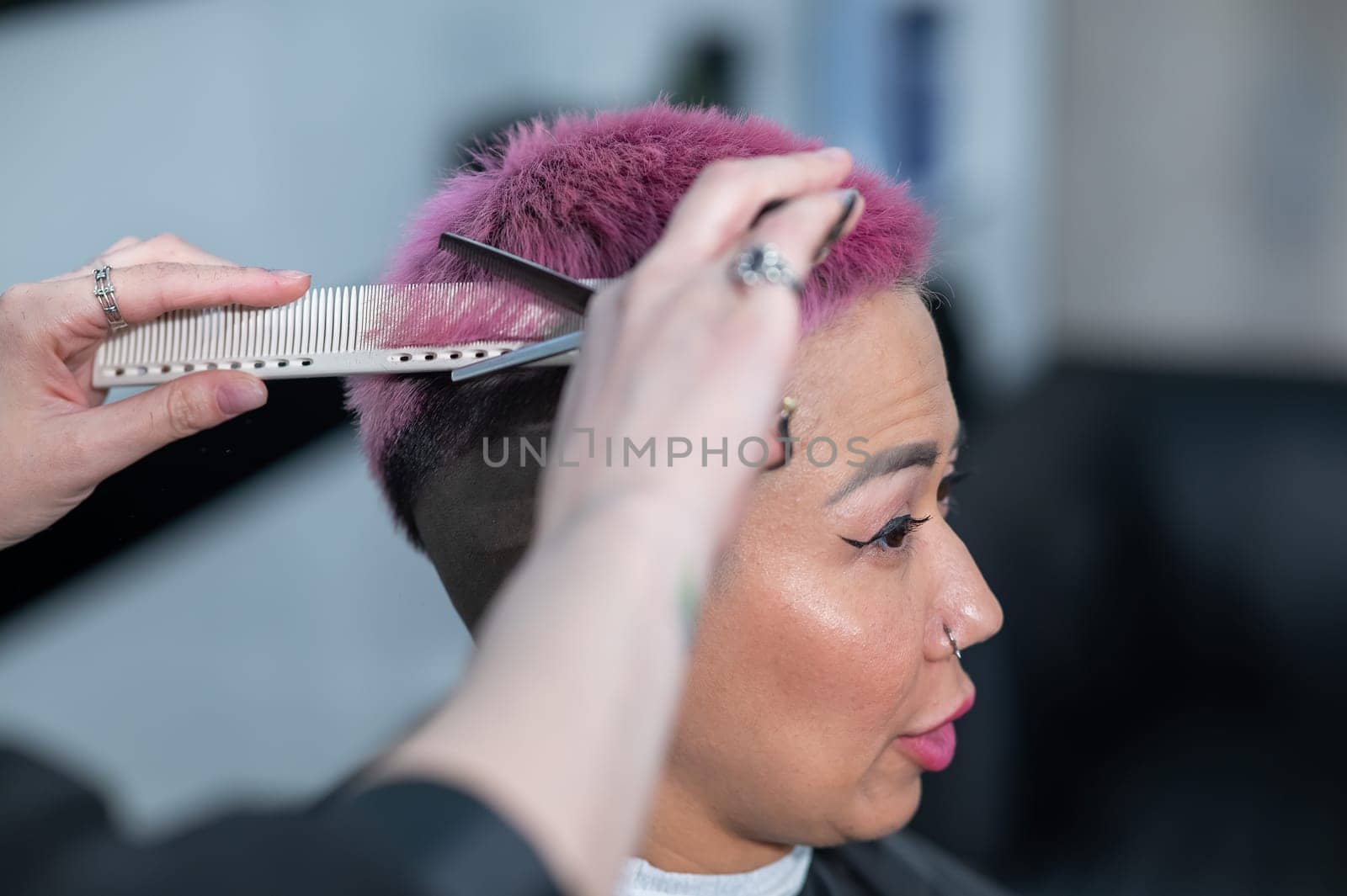 Hairdresser cuts Asian woman with short pink hair in barbershop. by mrwed54